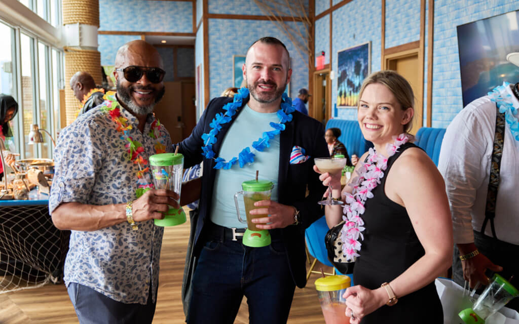 Three people smiling at the camera while wearing Hawaiian lei flowers around their necks while holding drinks in Margaritaville cups with straws